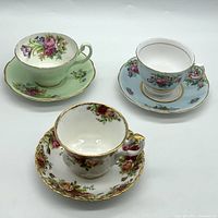 Three fine bone china tea cups and saucers displayed showing floral designs and gold trim.