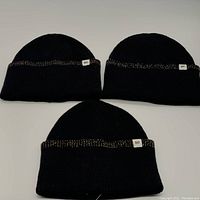 Photo of three black cuffed beanies side by side, showing the texture and BP fabric tag on the cuff.