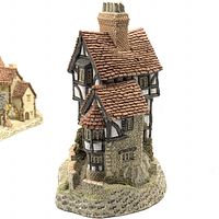 Side view of a David Winter cottage with detailed roof, chimneys, and stonework base.