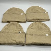 Lot of four beige BP oversized cuff beanies arranged in two rows against a white background, showing the wide cuff and knit pattern with BP logo tags.