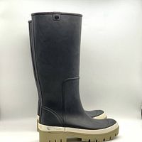 Side view of black Tory Burch tall boots with beige and light brown sole, showing height and logo.