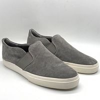 Pair of grey suede perforated slip-on sneakers with white soles angled front view.