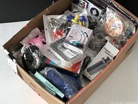 Box filled with various new items including small packaged tools, lights, headgear, and cables
