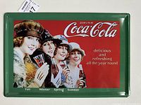 Photo of the first Coca-Cola tin sign featuring four women with the seasons Fall and Winter labeled below, on a green-framed metal sign measuring approximately 20cm by 30cm.