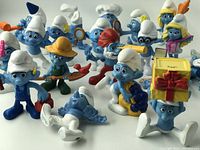 Group photo of 22 Smurf collectible figures in various poses including one holding a gift box, one with a telescope, and one wearing a straw hat with a fishing pole.