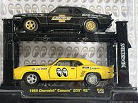 Front view of two 1969 Chevrolet Camaro Z/28 RS diecast models in black and yellow, inside original unopened packaging labeled with Mooneyes branding.