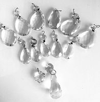 Full view of 15 vintage clear crystal chandelier prisms with various teardrop shapes and sizes along with metal hooks attached.