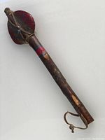 Full view of the vintage tomahawk showing wooden handle with painted stripes and leather wrapped stone head with feather design in blue and gold.