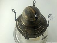 Close-up of metal top with wick holder and company inscription.