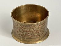 Side view of cylindrical brass pot showing the full etched floral pattern with red enamel background around the leaves.