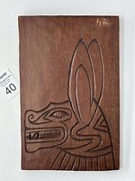 Front view of the rectangular wooden plaque carved with a stylized First Nations animal head design in relief and incised lines.