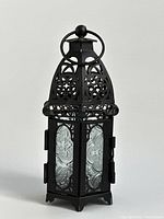 Front angle view of black metal patio lantern with closed door, showing decorative glass and metalwork.
