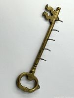 Close-up of large vintage brass key-shaped key holder showing the bow and five metal hooks along shaft.