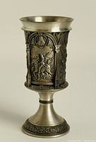 Front and side views of the pewter chalice showing four decorative relief panels with scenes inspired by Albrecht Durer's artwork. The chalice has ornate borders and a flared rim with a tapered stem and broad base decorated with floral or scrollwork patterns.