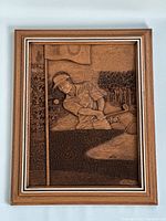 Full view of wood relief carving framed showing golfer near flagstick, golf ball, and natural scenery.