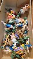 Top view of assorted Alice in Wonderland figurines in a cardboard box showing multiple characters including Alice and rabbits
