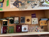 Overview of various costume jewelry items including necklaces, pins, earrings, and cufflinks arranged in two rows