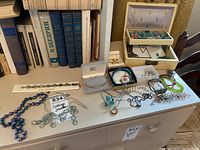 Overview photo of various necklaces, bracelets, and pins arranged on a table with books behind them.