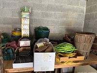 Jiffy pots, baskets, plastic edging, extension cords, watering cans, and buckets arranged on a wooden shelf against cinder block wall