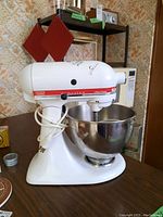 Side view of the white KitchenAid Ultra Power stand mixer with stainless steel bowl placed on a table, showing the red stripe and branding.
