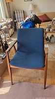 Front view of teak wood mid-century modern style armchair with blue upholstery in living room setting.