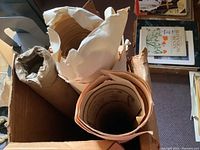 Top view of box showing multiple rolled posters and prints inside, some on brown and some on white paper.