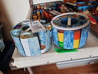 Two blue swirl plastic carousel holders for vintage pogs on a table, one filled mainly with hockey-themed pogs and the other with cars and military/spaces scenes
