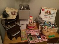 Wide view of the collection on a small table showing Smurf figurines, clown music boxes, finger puppets, miniature pianos, and the boxed Holly Hobbie gramophone toy.