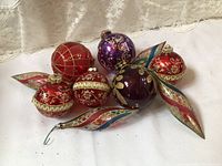 Seven vintage glass Christmas ornaments including five round baubles and two elongated swirl-shaped ornaments in red, purple, and gold.