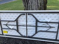Underside of the banquet table showing black folding metal legs attached to the plastic composite top. Legs are folded flat against the underside for storage.