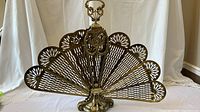 Front view of gold tone metal fan-shaped fireplace insert with ornate detail and pierced fan panels.