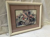 Angle view showing entire framed floral print in white ribbed wooden frame on a fabric backdrop.