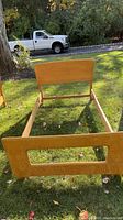 Front view of twin size bed frame showing headboard, footboard, and side rails on grass outdoors.