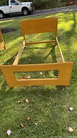 Photo of honey-colored wooden twin bed frame on grass, showing footboard with rectangular cutout design and solid wood construction