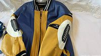 Blue and gold leather varsity jacket laid flat, showing front and sleeve designs.