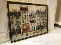 Framed art print showing Paris street scene with buildings and people, leaning against a surface.