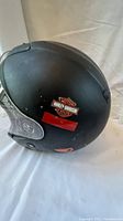 Side view of black helmet showing Harley-Davidson sticker and minor surface scuffs.