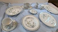 Wide view of multiple china pieces on a grey cloth, showing oval platters, cups, saucers, and small serving dishes with floral designs.