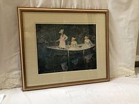 Framed artwork showing overall view of the print in wooden frame with gold trim and beige matting, set against a white fabric backdrop.