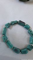 Turquoise stone bracelet with irregular rectangular beads and silver-tone spacers photographed on white surface.