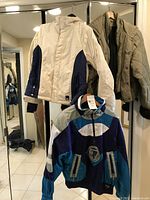 Three jackets hanging on rack: beige casual jacket with blue side panels, blue and purple Tyrolia ski jacket, and olive green quilted jacket by American Eagle Outfitter.