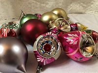 Varied vintage glass Christmas ornaments in multiple colors and shapes arranged on a lace background.