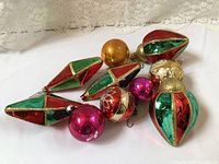Seven assorted vintage glass Christmas ornaments arranged on white fabric background under lace curtain