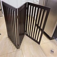 Full view of the three-panel foldable baby or pet gate in dark wood on tiled floor near kitchen appliances.