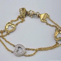 Close-up image showing the gold and silver heart-shaped charms and lobster clasp of the bracelet.