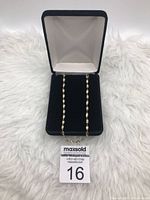 Chain necklace displayed inside an open black velvet jewelry box with white interior lining on a white textured background.