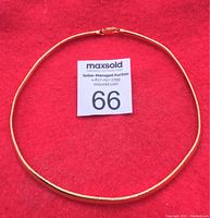 Gold plated silver omega chain necklace laid flat on red background with auction label '66'. Shows full necklace and clasp.