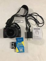 Photo of Nikon D40 camera with battery, battery charger, power cord, and camera strap laid out on white surface.