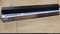 Philips black soundbar shown resting on its original blue and white box on a beige floor.