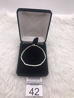 Sterling silver bracelet displayed inside black velvet-lined jewelry box on a white furry surface.
